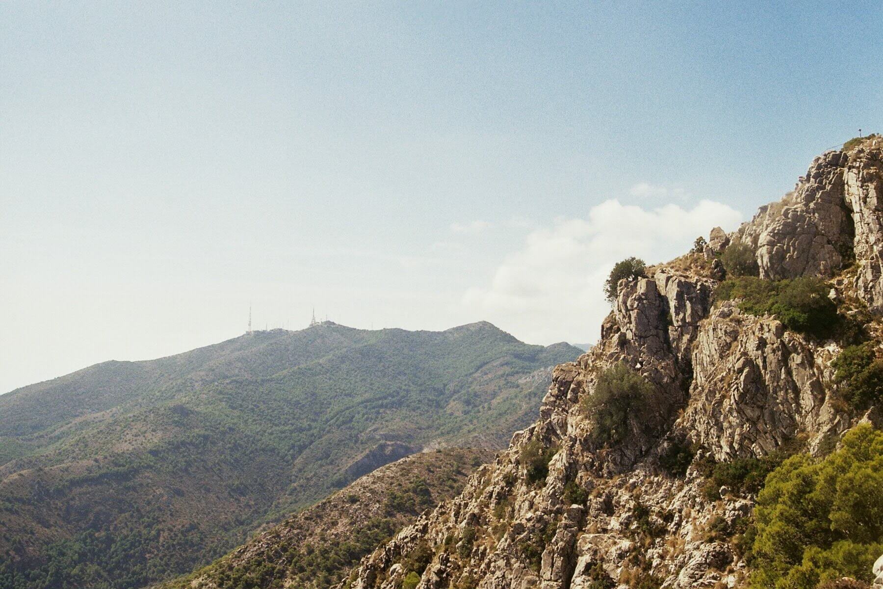 Kesämaisema, jossa kivinen vuorenseinä kuvassa.