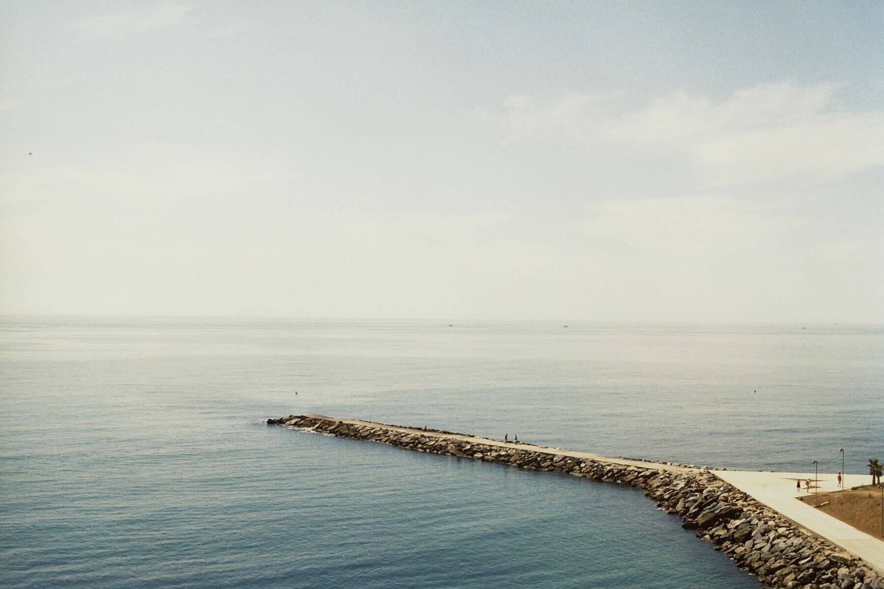 Landskap mot havet med en stenig pir i bildets nederdel
