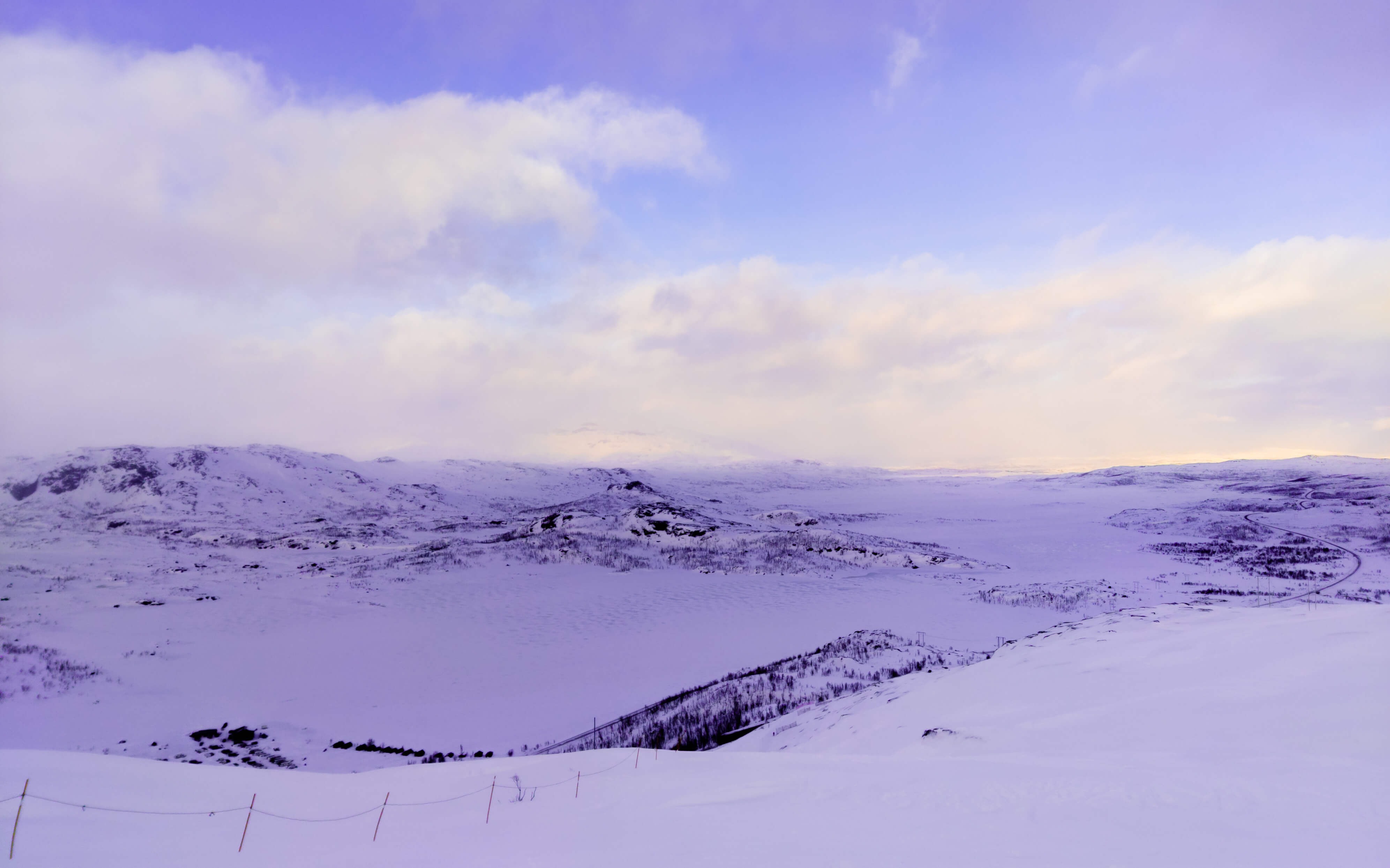Photo from the top of a mountain in winter towards a valley with mountanous terrain on the other side